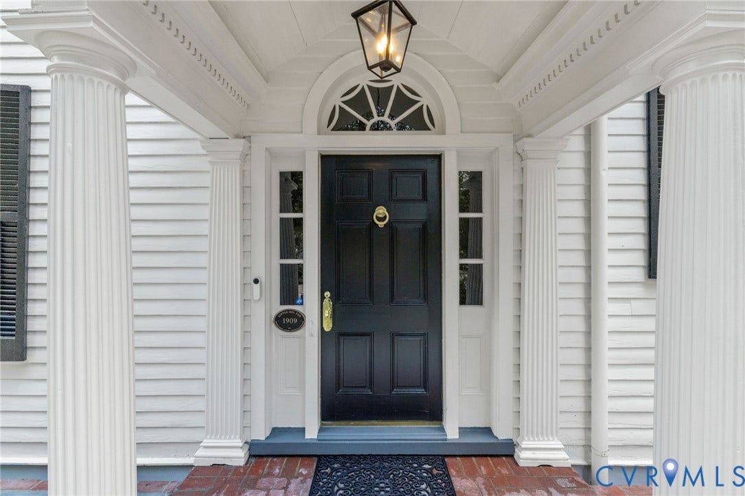Entryway featuring a black paneled door, decorative transom window, and fluted columns
