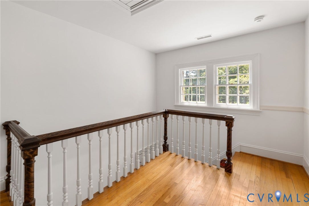 Hardwood flooring, painted white walls, two double-hung windows, and a classic balustrade with a wood-finish handrail