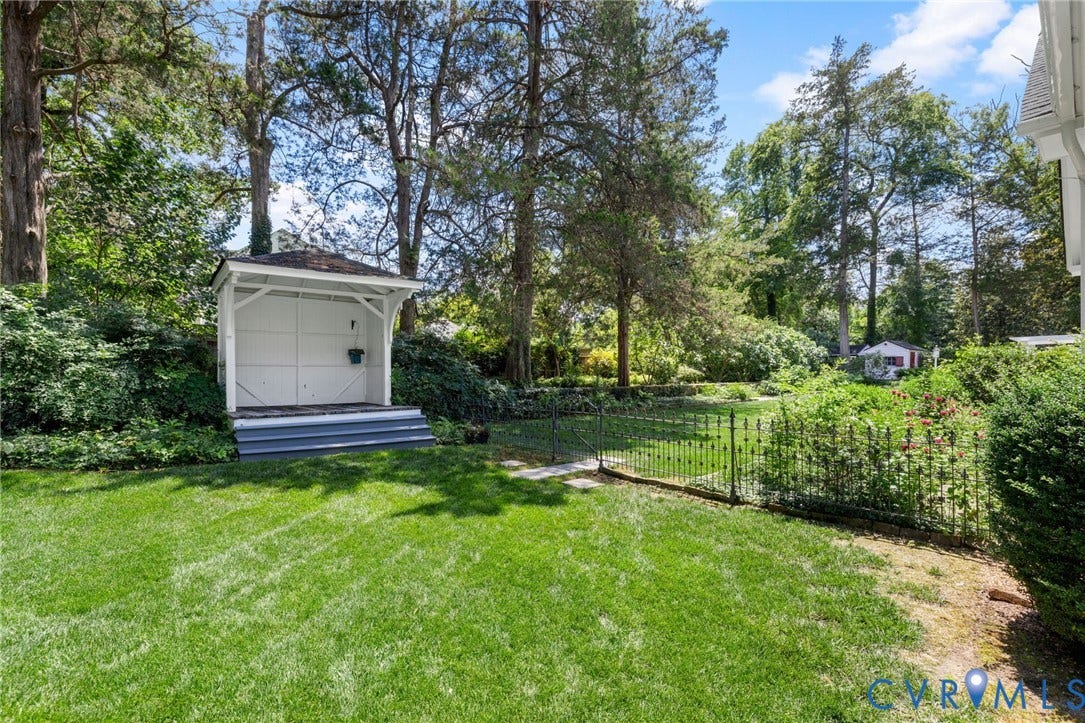 Manicured lawn, mature trees, white garden shed with shingle roof, wrought iron fencing, and established perimeter plantings