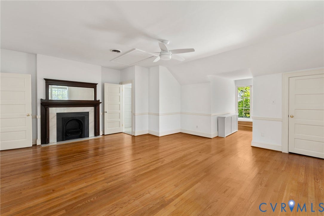 Hardwood flooring throughout, a decorative fireplace with a dark wood mantel and marble-like surround, a ceiling fan, white paneled doors, and a window providing natural illumination