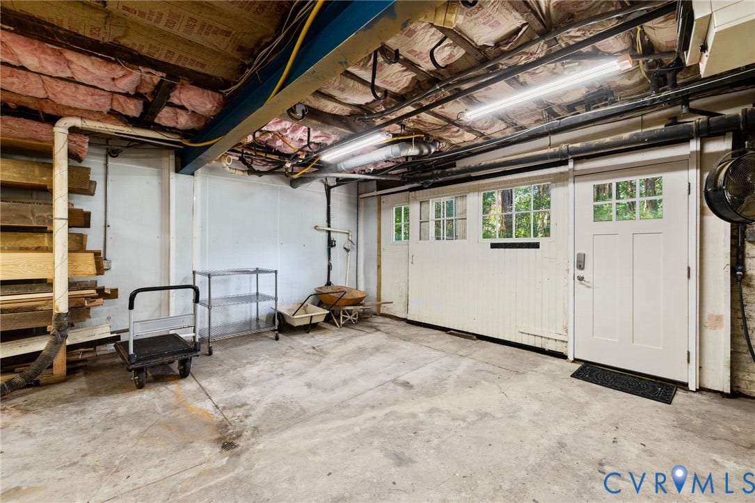 Concrete flooring, exposed ceiling joists, white paneled garage door with windows, white side entry door with windows, fluorescent overhead lighting