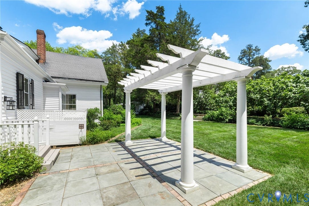 White pergola with classical columns, flagstone patio, brick border, and lush lawn