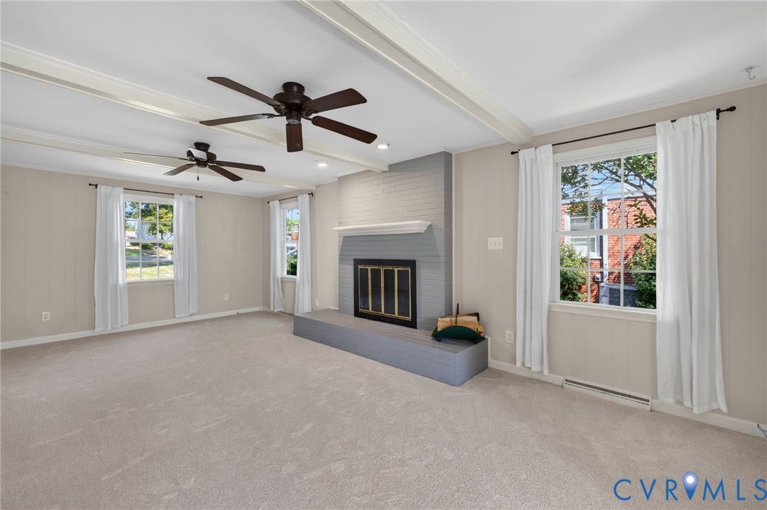 8415 Holly Hill Road, Henrico, VA 23229 Spacious living area featuring exposed beam ceilings, two ceiling fans, a brick-surround fireplace with a mantel, and two windows