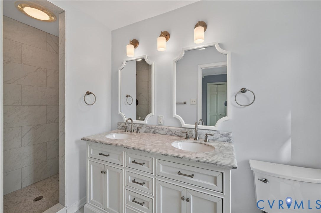 8415 Holly Hill Road, Henrico, VA 23229 Dual vanity with white cabinetry, stone countertop, two undermount sinks, and decorative mirrors