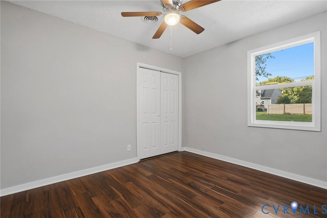 Wood-finish flooring, light gray wall paint, a window with a white frame, and a ceiling fan with integrated lighting