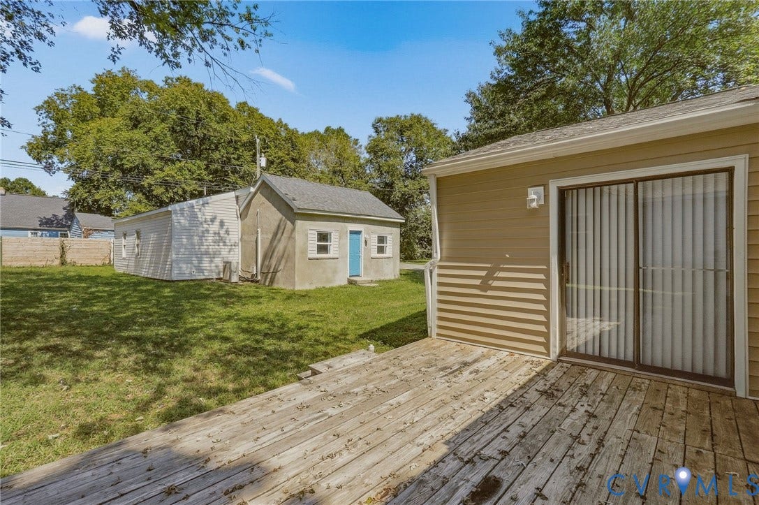 Rear deck with sliding glass door, tan horizontal siding, and a detached structure with a light blue door