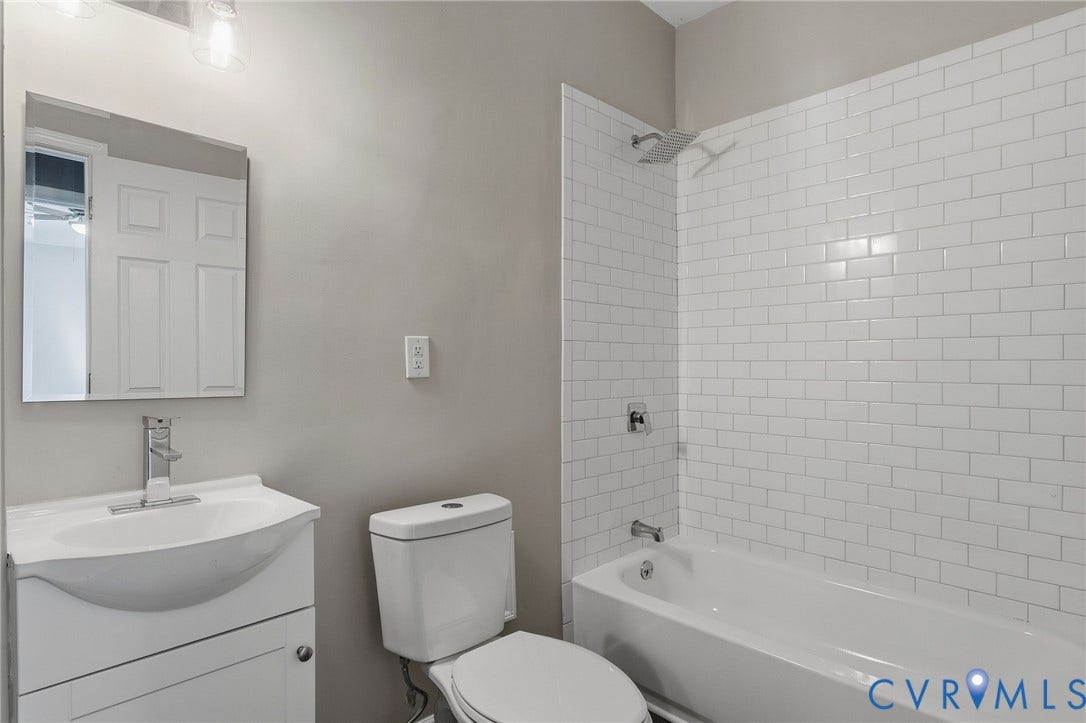Bathroom featuring a white vanity with integrated sink, chrome faucet, white subway tile shower surround, and a rain showerhead