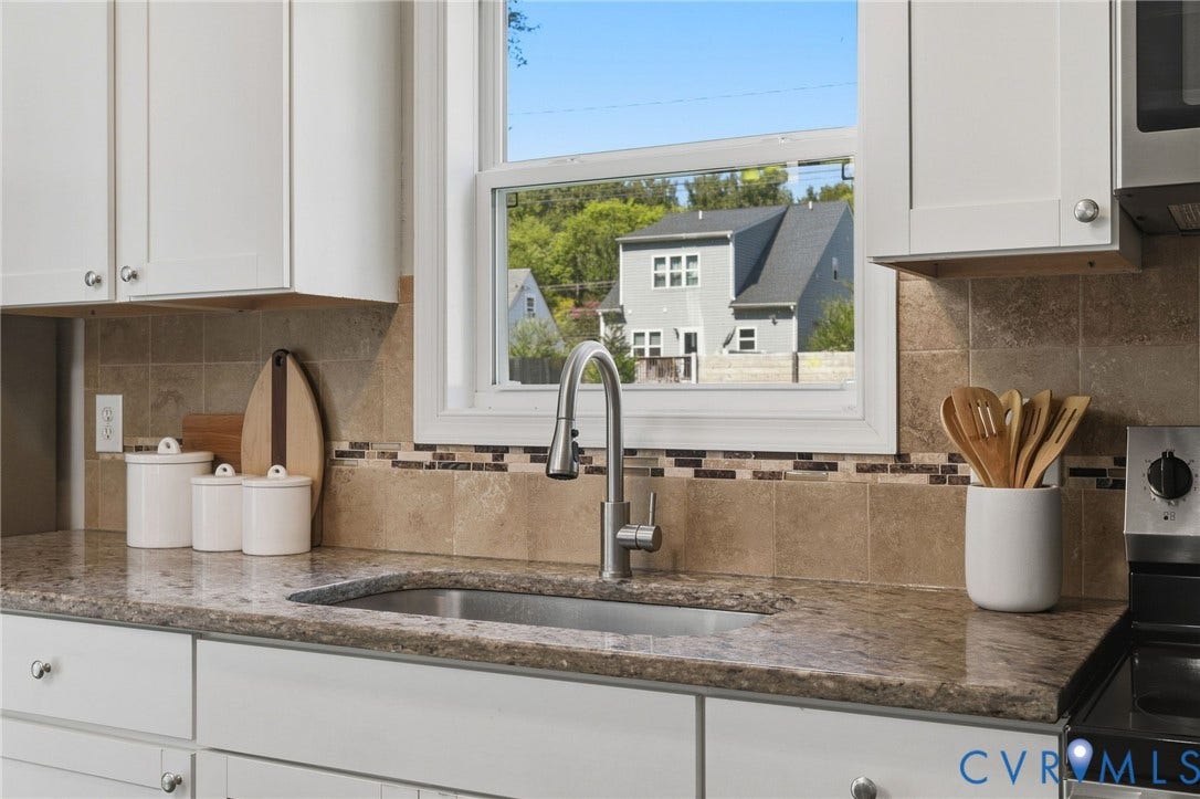 White shaker-style cabinetry, a stainless steel sink, a modern pull-down faucet, and a tiled backsplash with mosaic accents, all complemented by stone countertops