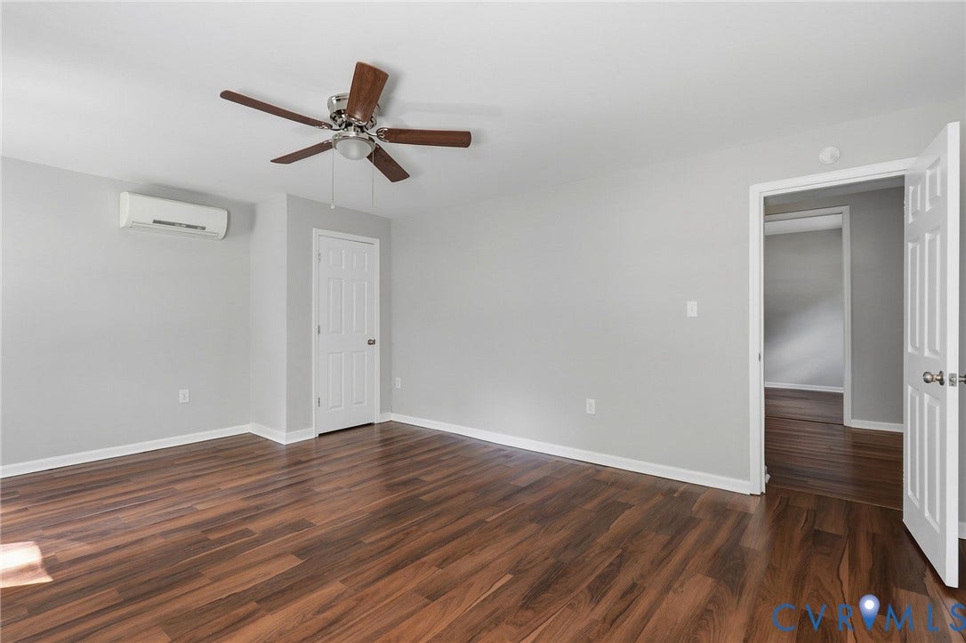 Spacious room featuring wood-finish flooring, light gray walls, a ceiling fan, and a wall-mounted AC unit
