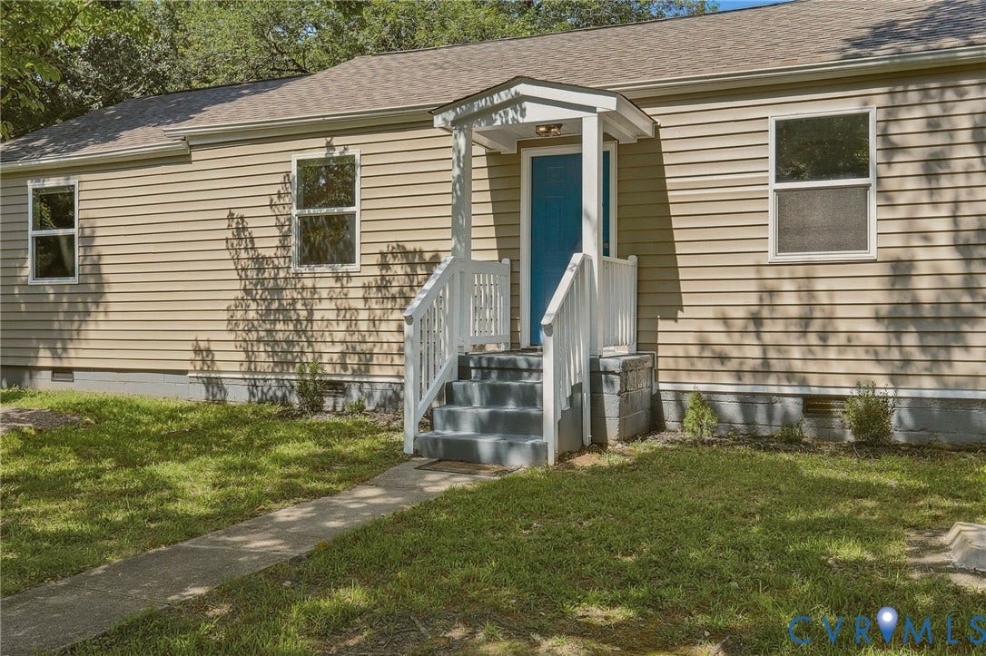 Beige horizontal siding exterior with a light blue entry door, white railings, and a concrete pathway