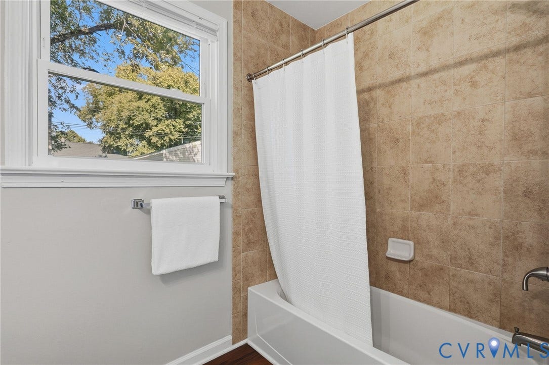 White framed window, tiled shower surround, bathtub, and wood-finish flooring