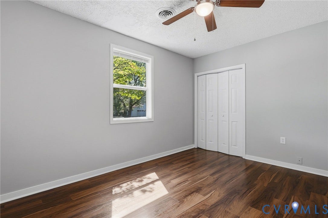 Wood-finish flooring, white bi-fold closet doors, white trim, white window frame, and a ceiling fan
