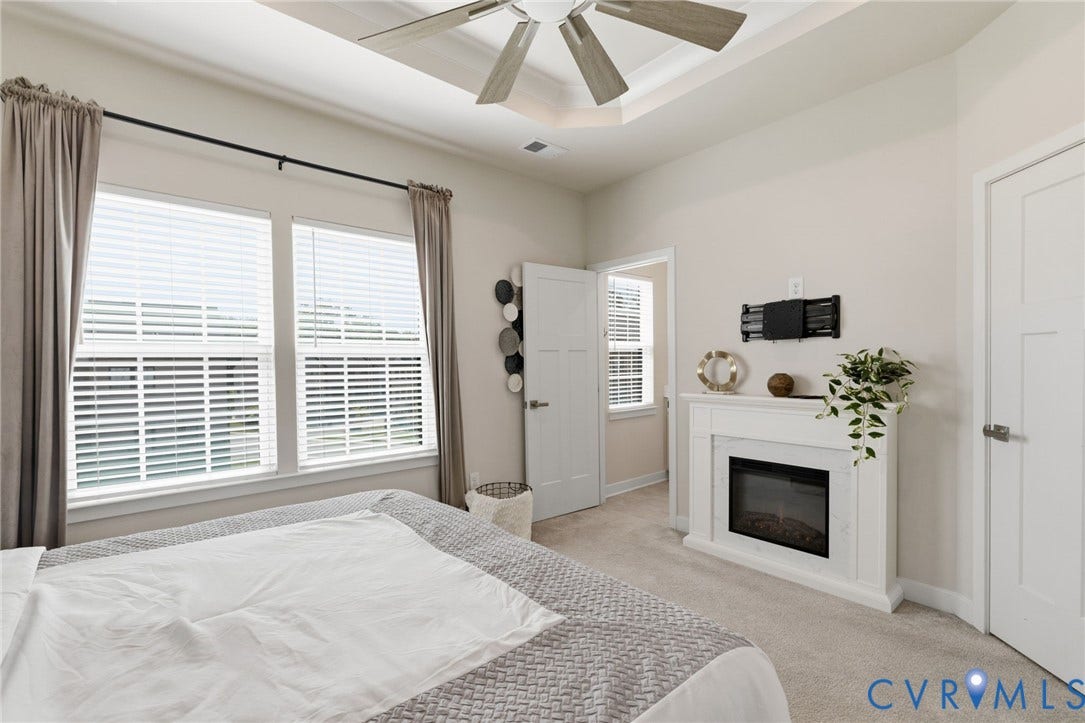 Tray ceiling with a ceiling fan, two windows, a built-in electric fireplace with heat