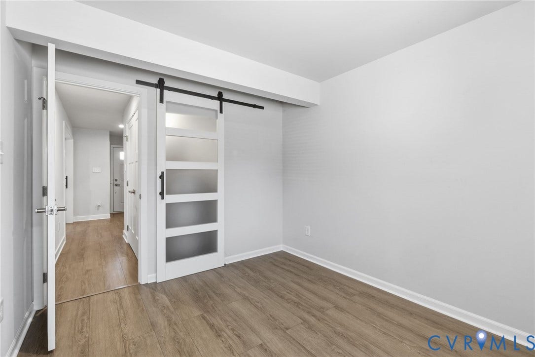 Wood-finish flooring throughout, and a barn door with frosted glass panels. Used as a mudroom with access door to the exterior of the home