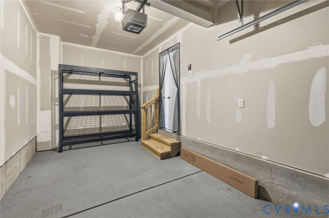 Single car garage with concrete fleck finished flooring and attached shelving that conveys