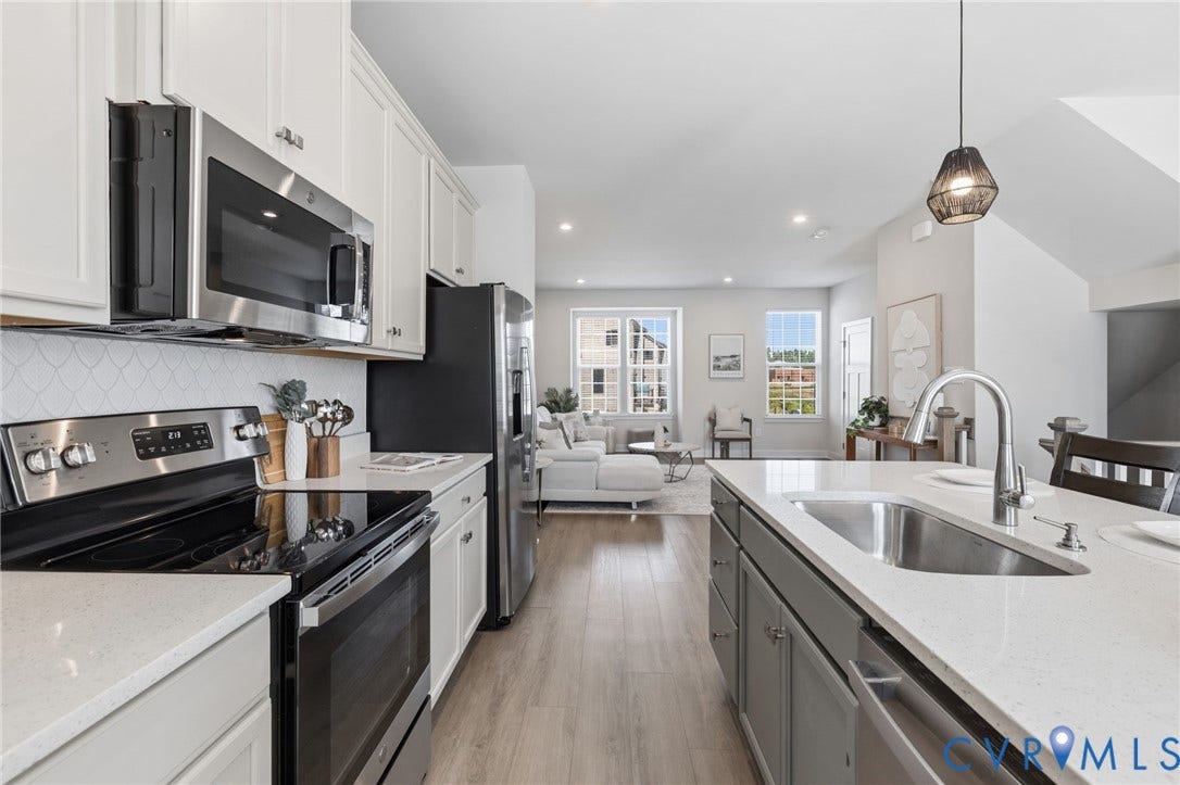Kitchen featuring stainless steel appliances, quartz countertops, white cabinetry, a custom tile backsplash, and a center island with a large farmhouse sink