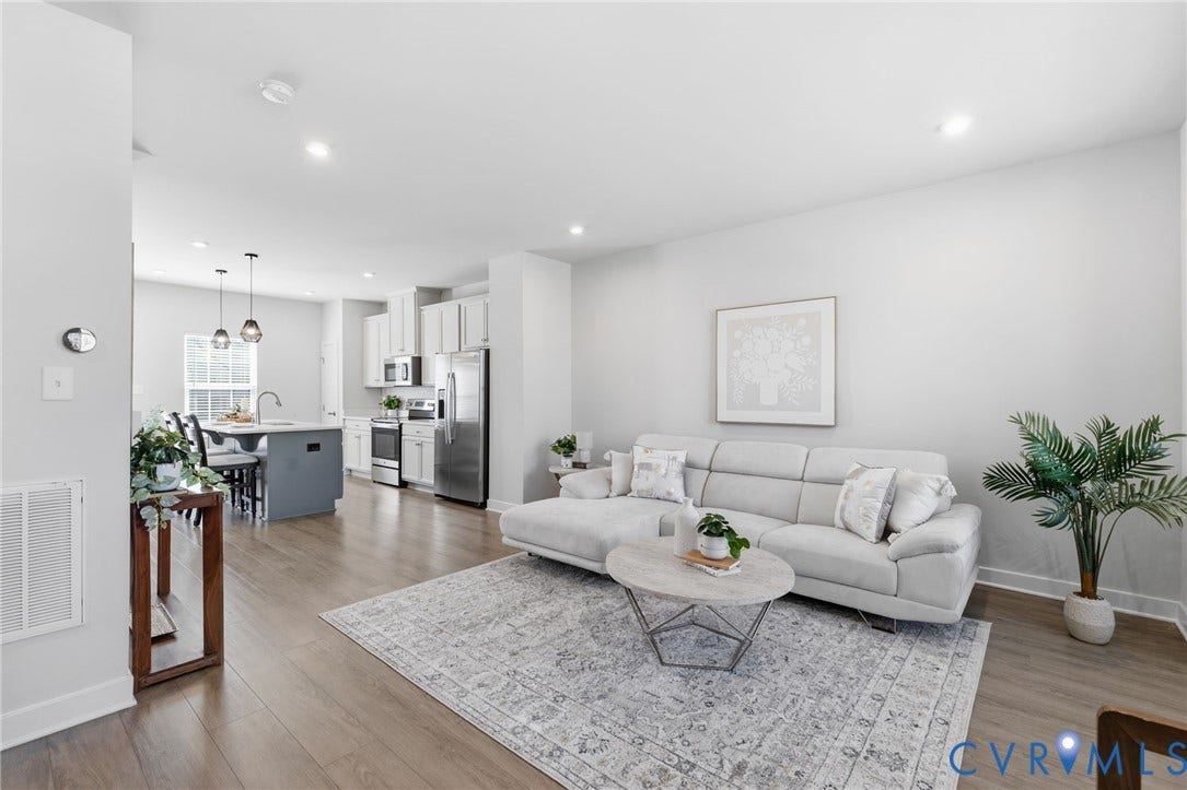Open-concept living area featuring wood-finish flooring, recessed lighting, and a kitchen with stainless steel appliances, white cabinetry, and a blue island with pendant lighting