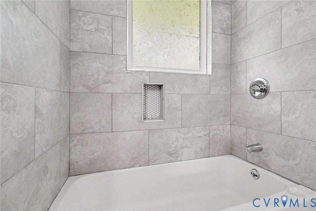Bathtub featuring tiled surround, integrated shower niche with mosaic tile, and chrome fixtures