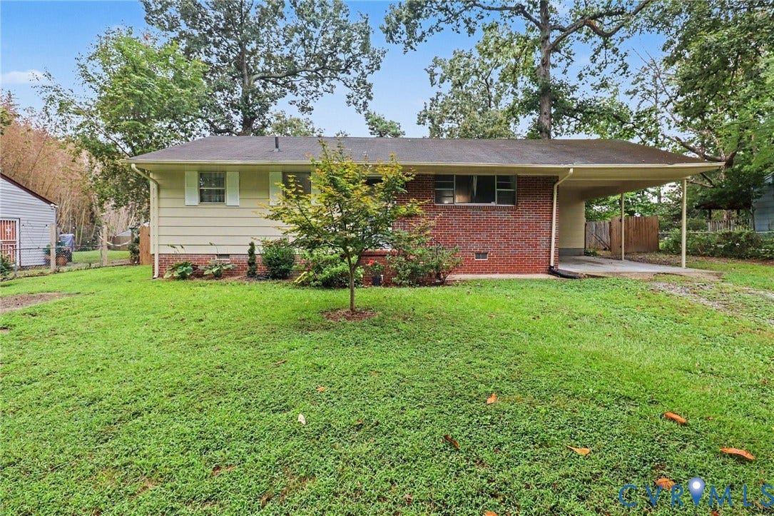 Brick and siding exterior with a covered carport, mature trees, and landscaping