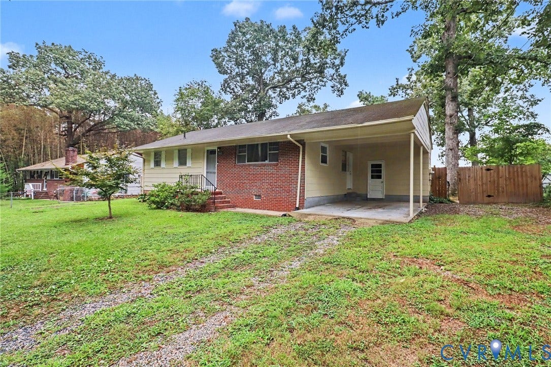 Brick and siding exterior with a covered carport, concrete steps, and a gravel driveway