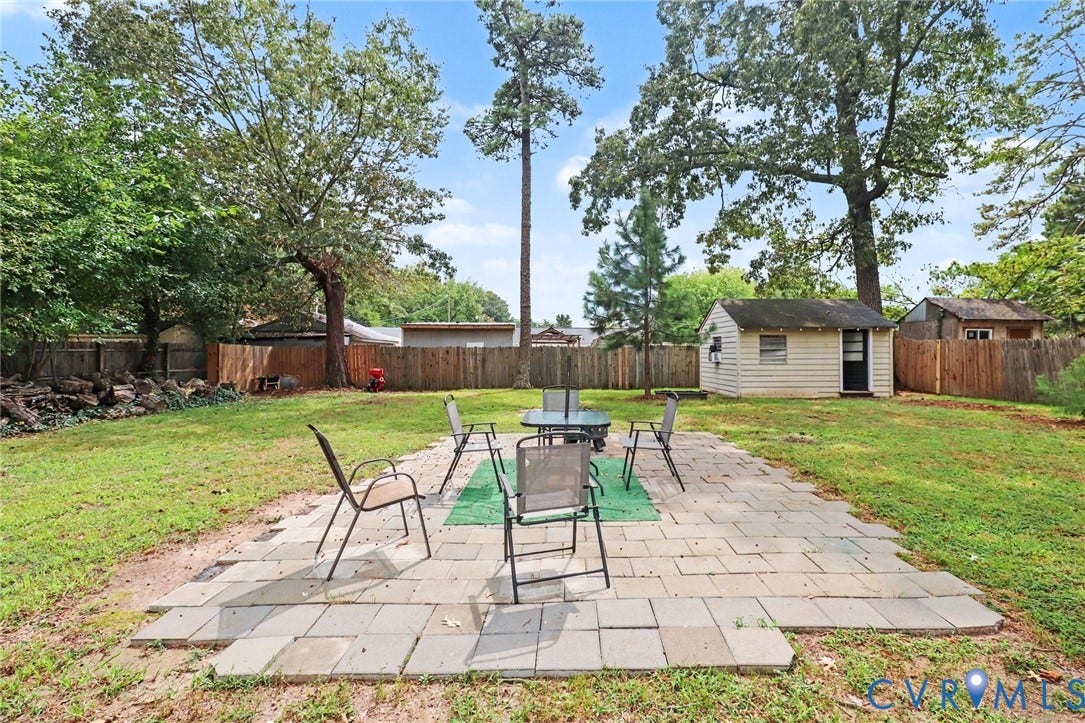 Expansive backyard featuring a concrete paver patio, a freestanding storage shed, and mature trees