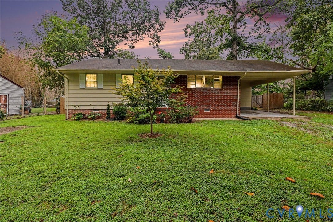 Single-story residence featuring brick and siding exterior, a covered carport, and a front lawn with mature trees