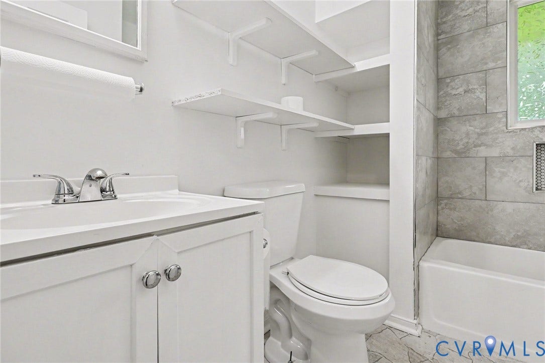 White vanity with chrome faucet and integrated sink, built-in shelving, white toilet, tiled shower with white bathtub, and patterned floor tile