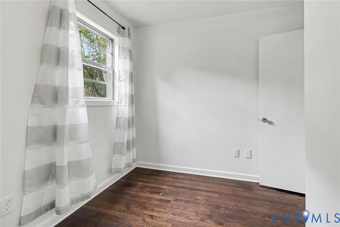 Dark wood-finish flooring with white baseboards, bright white walls, and a window with white trim