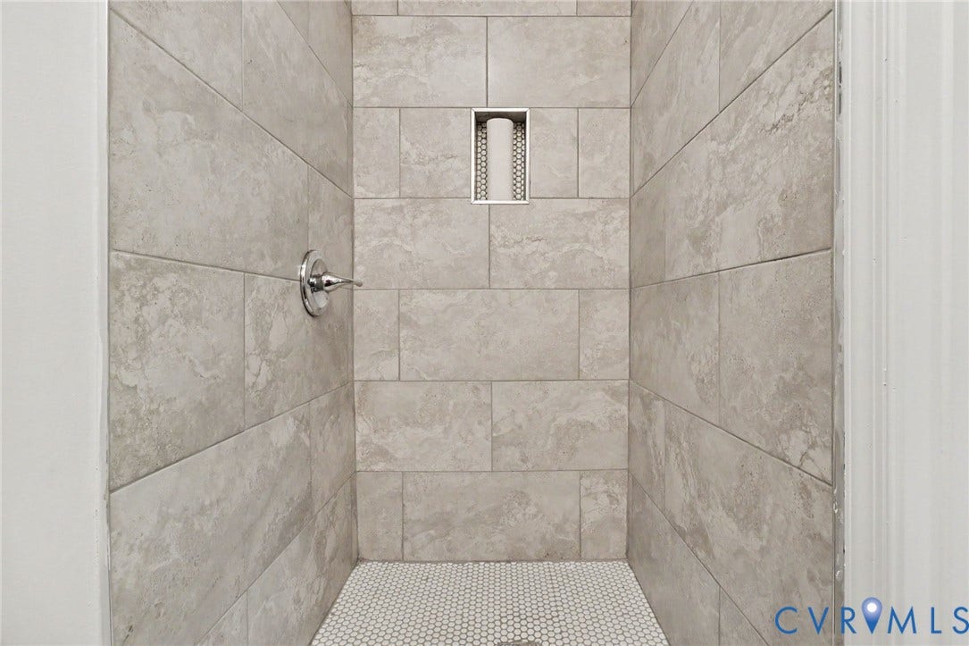 Shower with light-toned rectangular wall tiling, a built-in niche, and small hexagonal floor tiling