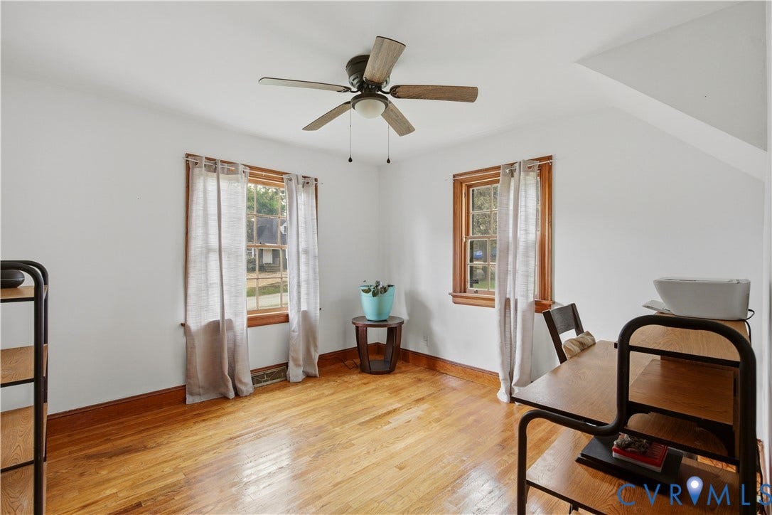 Natural hardwood flooring, multiple windows with natural wood trim, sloped ceiling detail, and a ceiling fan with integrated lighting