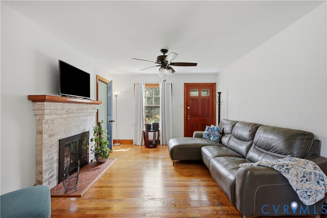 Hardwood flooring with a brick fireplace, a wood mantel, and a dark wood entry door