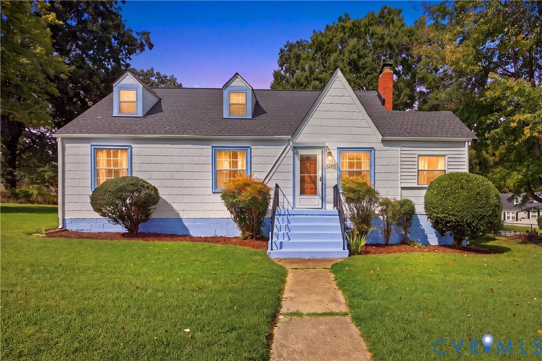Light blue exterior siding, dark roof shingles, two dormer windows, blue painted porch steps, and a red brick chimney