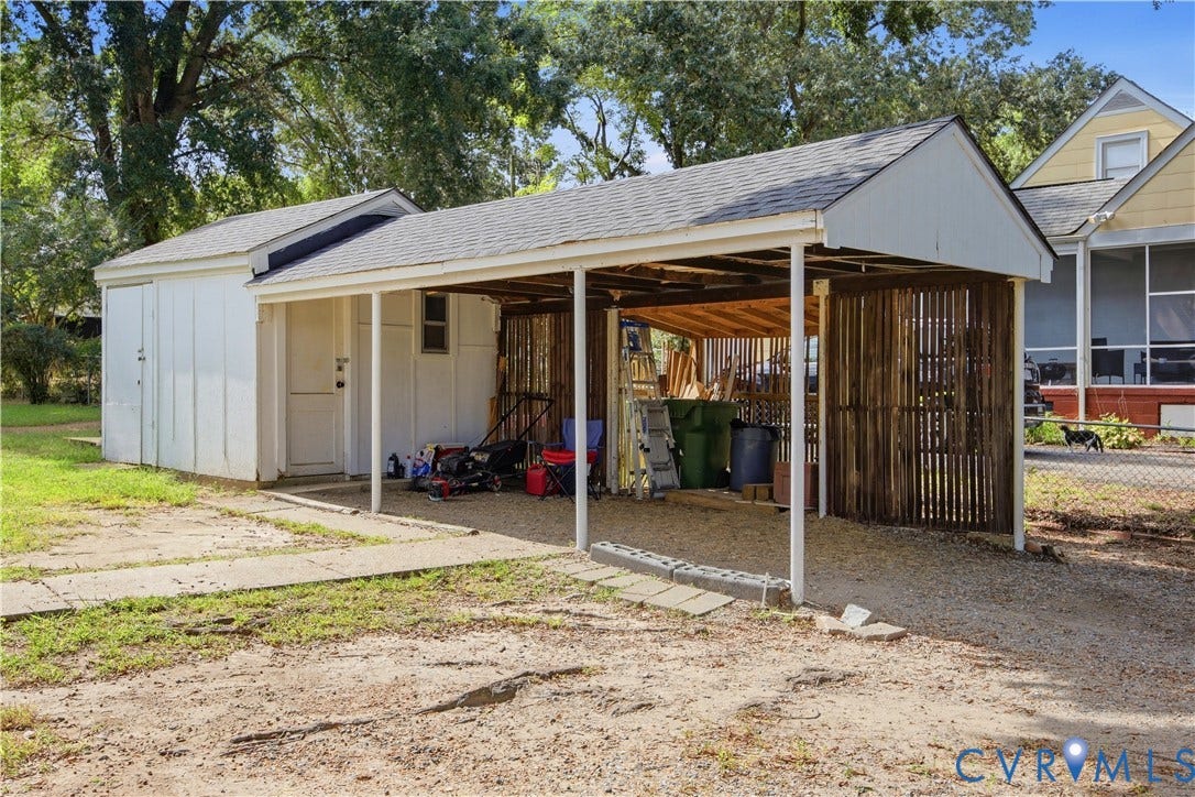 Detached shed structure with a carport, featuring a gabled roofline and a gravel surface