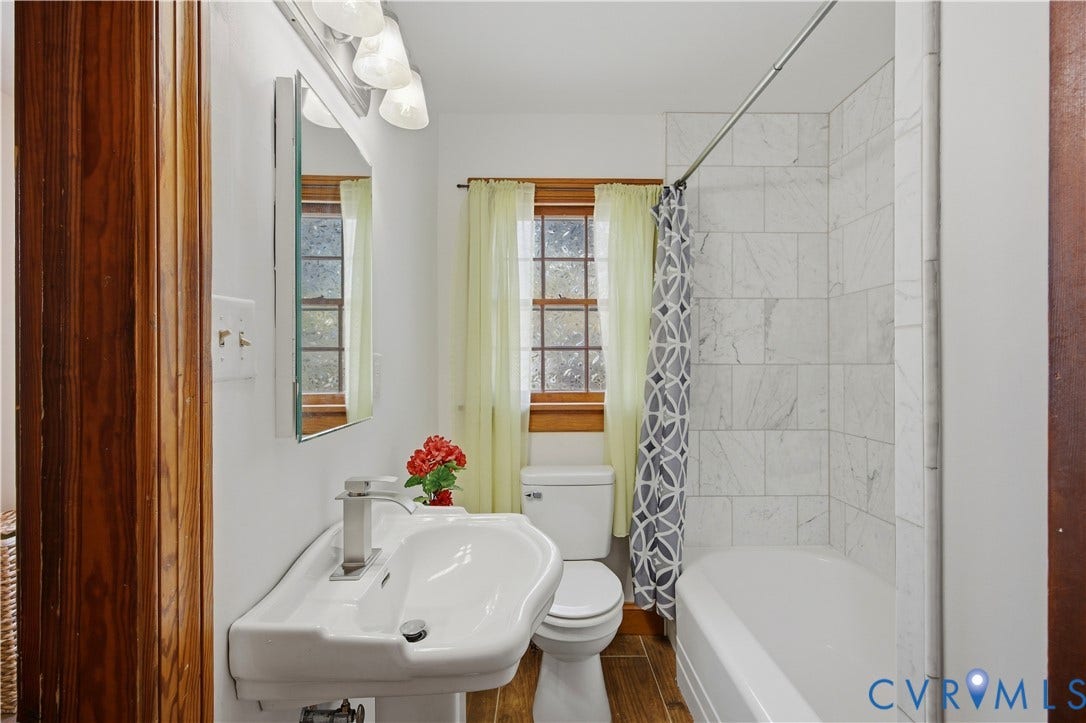Pedestal sink with a polished chrome faucet, white bathtub with a tiled surround, and wood-finish flooring