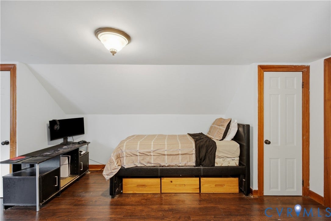 Wood-finish flooring with a white six-panel door, and a flush mount ceiling light fixture