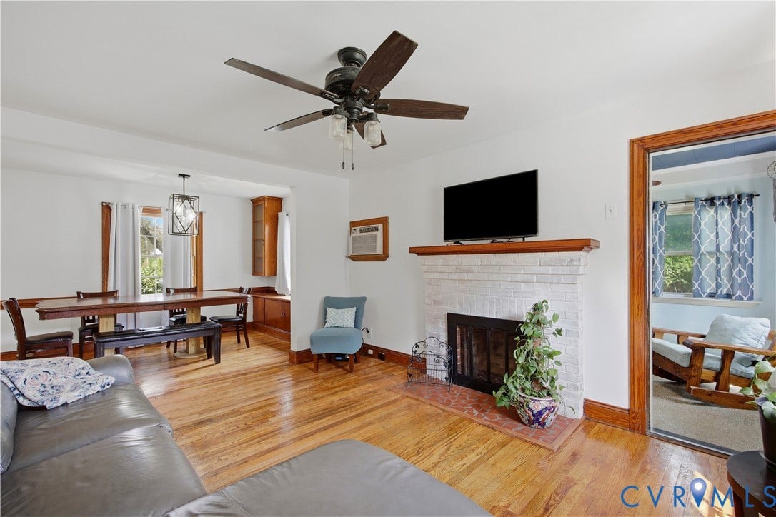 Hardwood flooring throughout, white brick fireplace with mantel, built-in cabinetry, and a ceiling fan