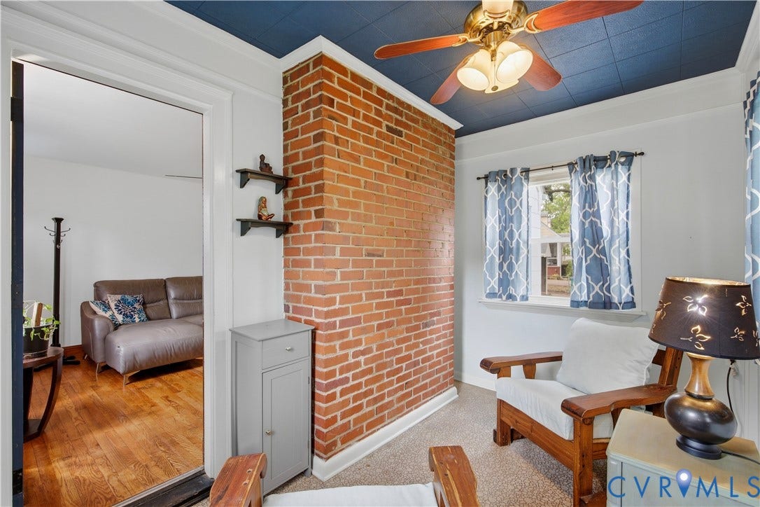 Exposed brick wall with built-in shelving, wood-finish ceiling fan with lighting, and light-colored flooring