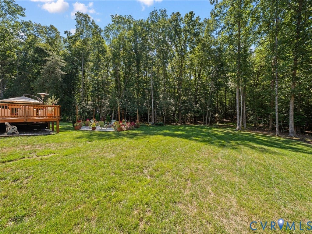 5927 Trenholm Village Drive, Trenholm Village, Powhatan, VA 23139 Expansive grassy lawn with a wood-finish deck featuring a built-in pergola and a stone-paver patio, all surrounded by mature trees