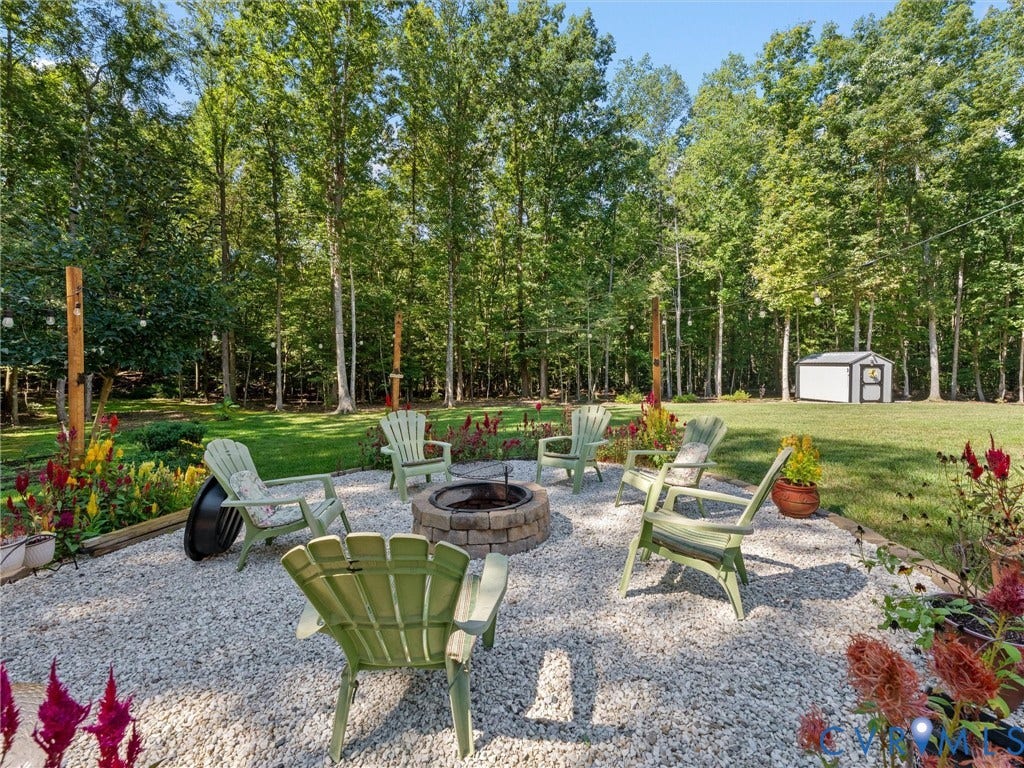 5927 Trenholm Village Drive, Trenholm Village, Powhatan, VA 23139 Gravel patio with a built-in fire pit, surrounded by lush green lawn and mature trees