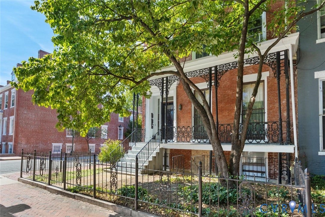 Front yard bordered by wrought iron fence and shaded by a mature dogwood.