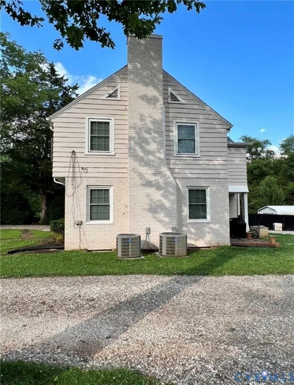 13232 W James Anderson Highway, Courthouse Area, Buckingham, VA 23921 Exterior with vertical siding and brick facade, prominent chimney, multiple windows, two outdoor HVAC units, and a gravel surface