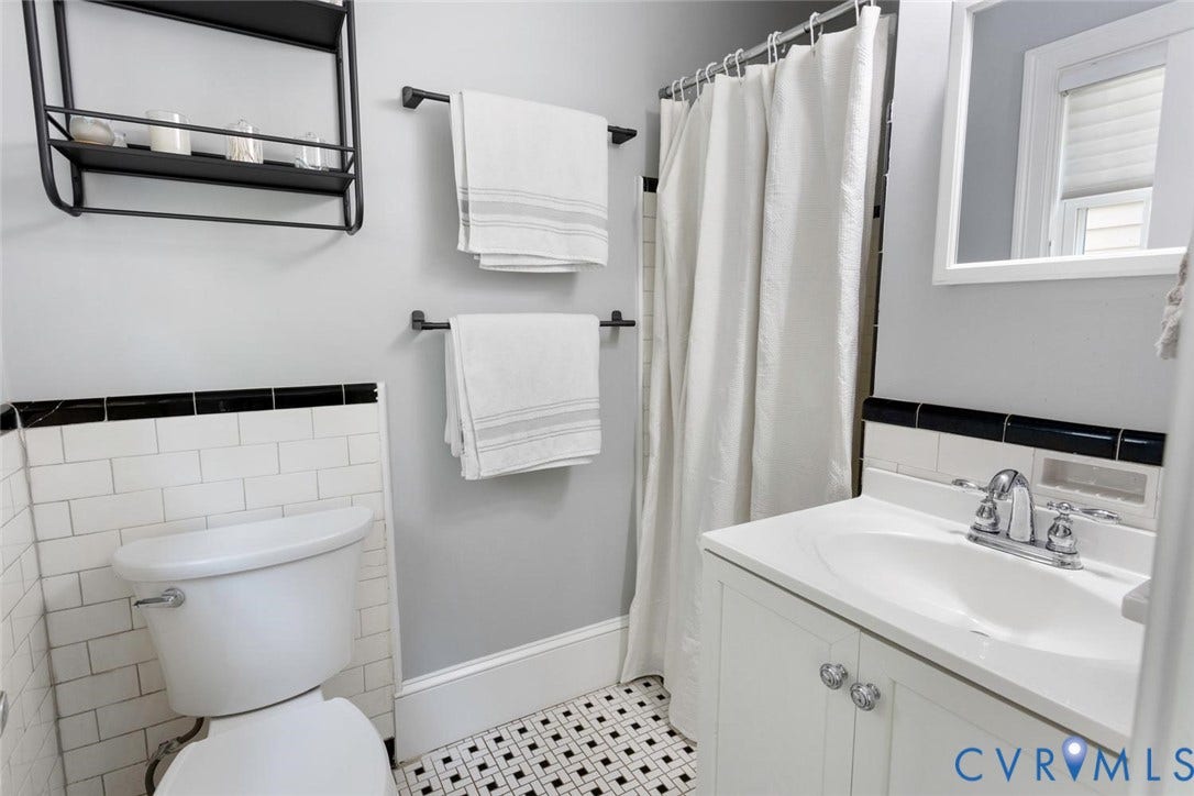5113 King William Road, Westover Hills, Richmond, VA 23225 White subway tile wainscoting with black trim, black and white geometric tile flooring, white vanity with integrated sink, chrome fixtures, and a wall-mounted shelving unit