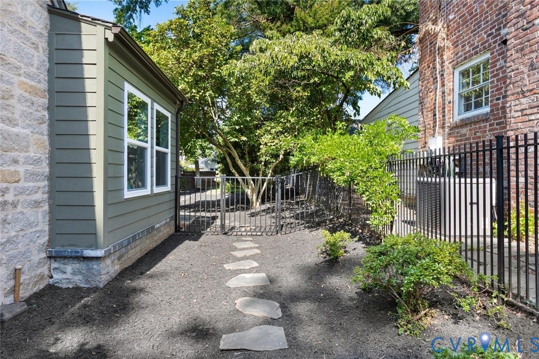 5113 King William Road, Westover Hills, Richmond, VA 23225 Stone and siding exterior with multiple windows, leading to an enclosed outdoor space featuring stepping stones, mature trees, and a black wrought iron fence