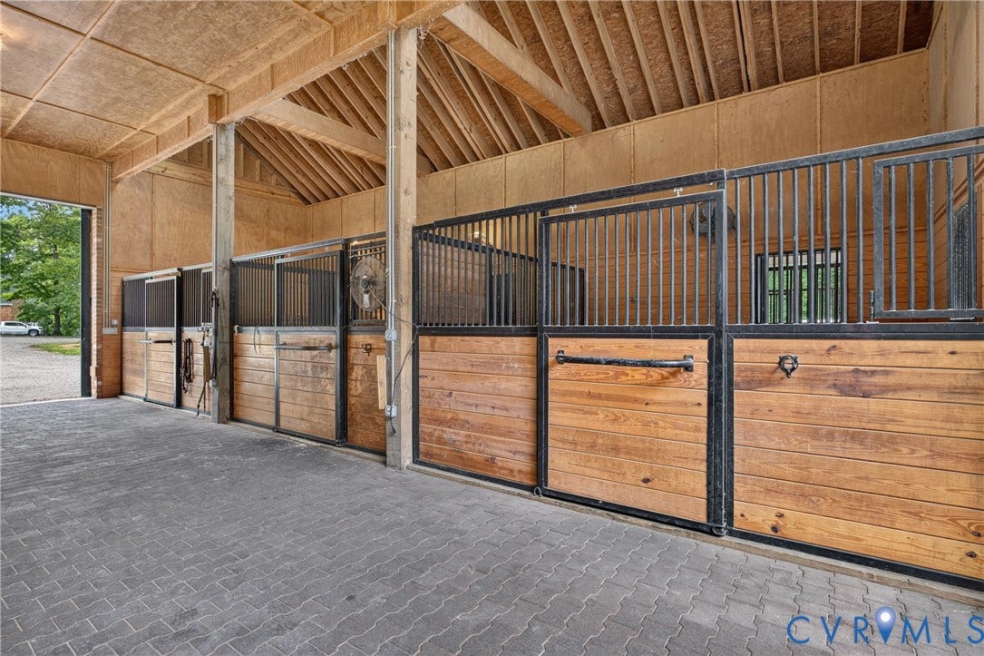 1108 Shallow Well Road, Manakin Sabot, VA 23103 Barn interior featuring exposed wood beams, multiple stalls with wood and metal construction, and a paved floor