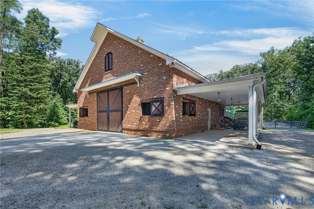 1108 Shallow Well Road, Manakin Sabot, VA 23103 Brick exterior barn structure featuring large sliding wooden doors, a covered carport, and a gravel driveway
