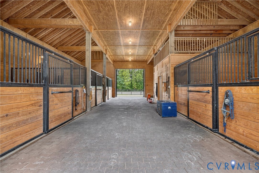 1108 Shallow Well Road, Manakin Sabot, VA 23103 Wood-paneled stable stalls with black metal grates, exposed wooden beams, and a second-story wooden railing overlooking the main floor