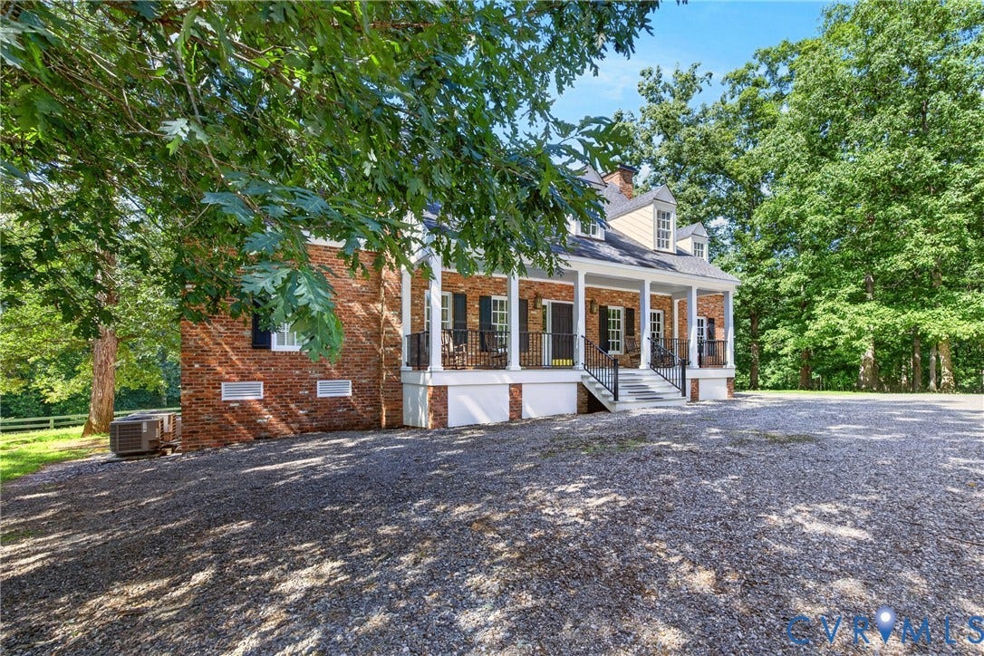 1108 Shallow Well Road, Manakin Sabot, VA 23103 Brick exterior with dormer windows, a full-width covered porch, white columns, black railings, and a gravel driveway