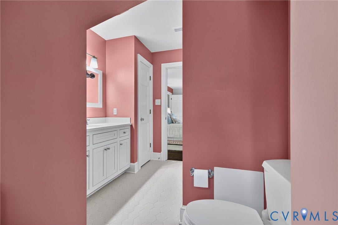 1108 Shallow Well Road, Manakin Sabot, VA 23103 White hexagonal floor tile, white vanity with cabinet storage, white rectangular sink, framed vanity mirror, and modern wall sconce