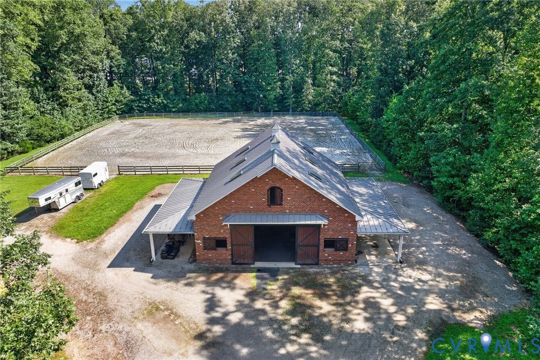 1108 Shallow Well Road, Manakin Sabot, VA 23103 Brick barn structure with a dark roof and multiple skylights, featuring an expansive outdoor riding arena with fencing, and gravel driveways