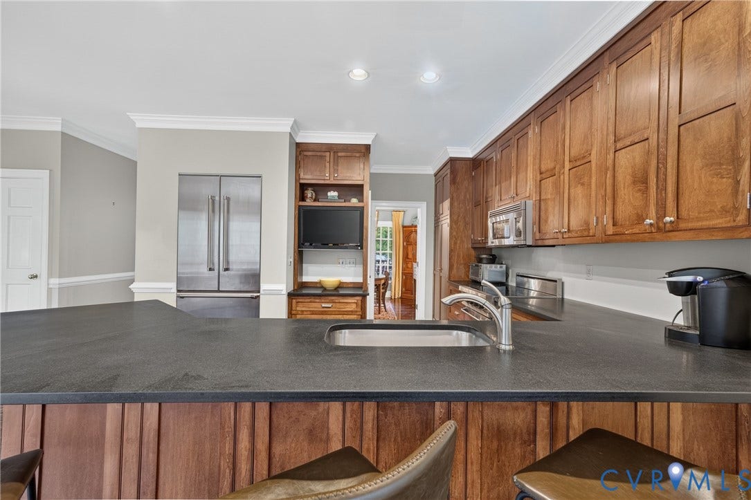 1108 Shallow Well Road, Manakin Sabot, VA 23103 Expansive kitchen island with a built-in sink, dark stone countertop, full-height wood cabinetry, stainless steel appliances, and integrated shelving